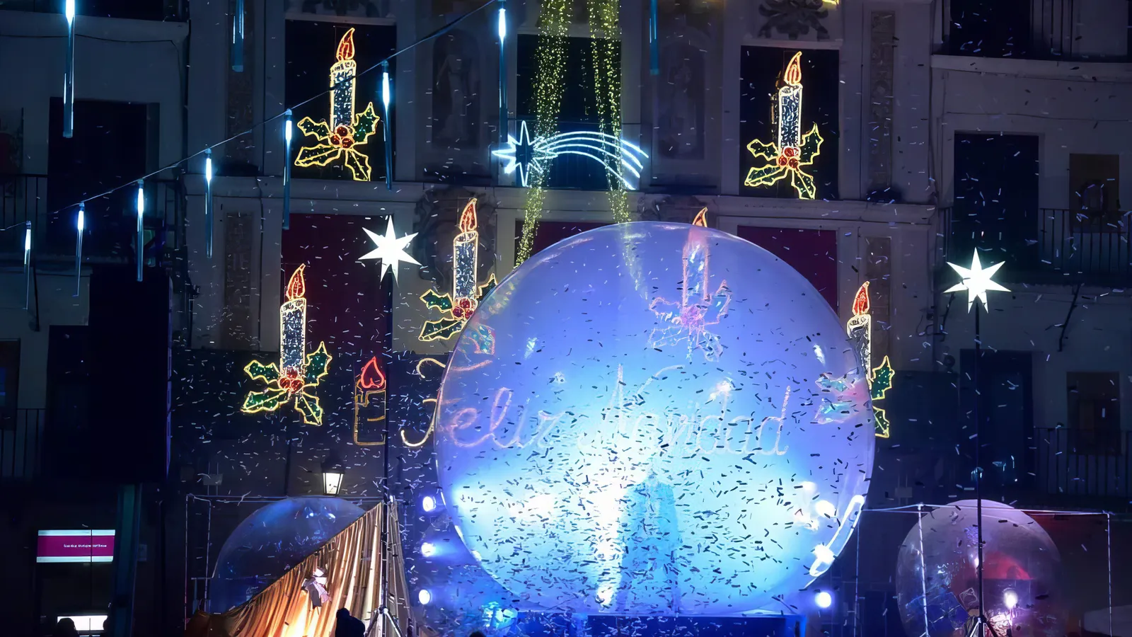 Lluvia de confeti sobre la esfera y la plaza, bajo el rótulo luminoso de Feliz Navidad ya encendido