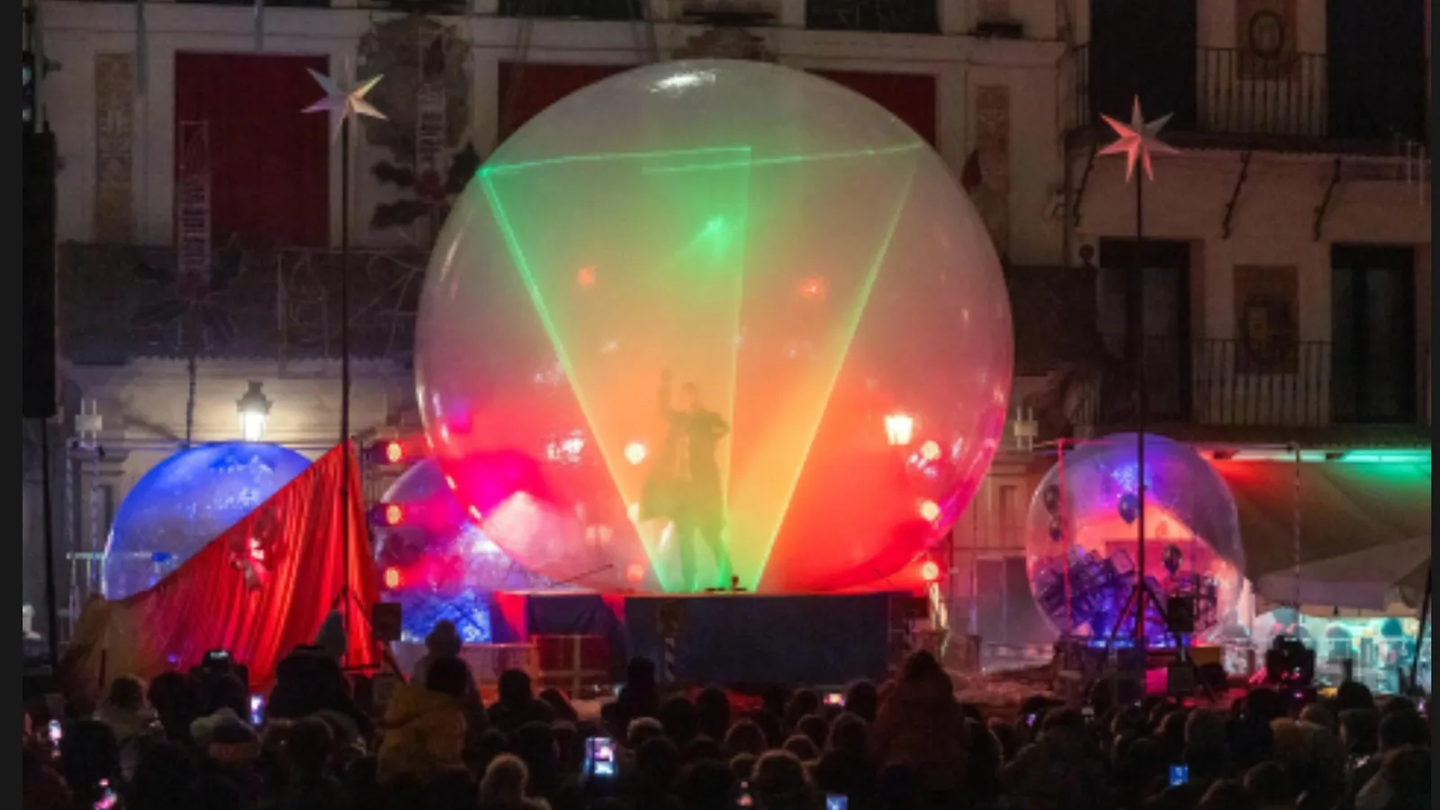 Haces láser formando un triángulo dentro de la esfera, con el público de la plaza grabando con el móvil
